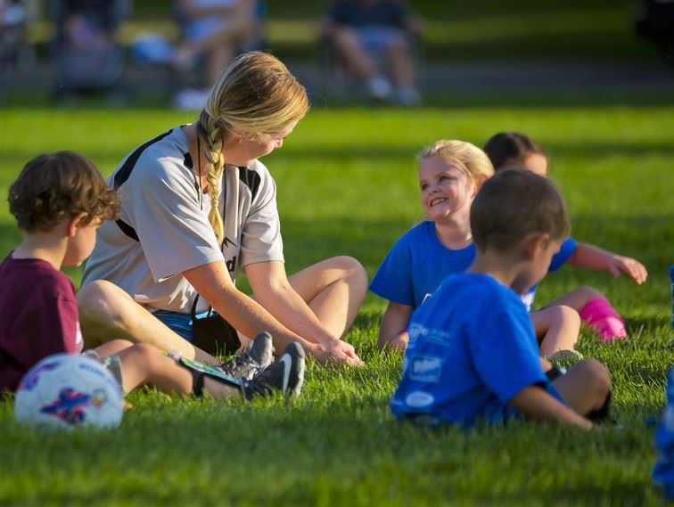Photo of a coach strecthing with her little striker's team