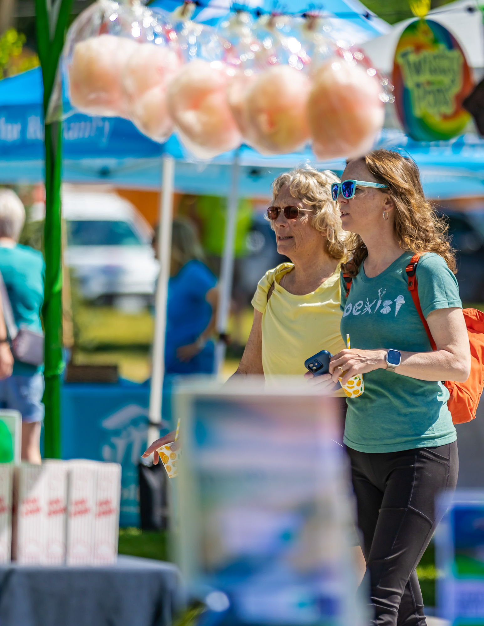 Crowd of people browsing vendor booths at the Berthoud Market in Town Park on a sunny Saturday.