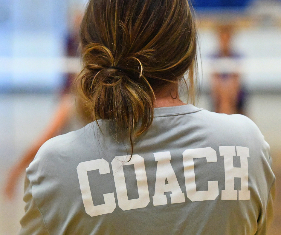 Female coach standing with her back to the camera, wearing a shirt that says COACH