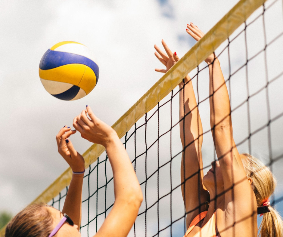 Two players reaching for a volleyball over a net