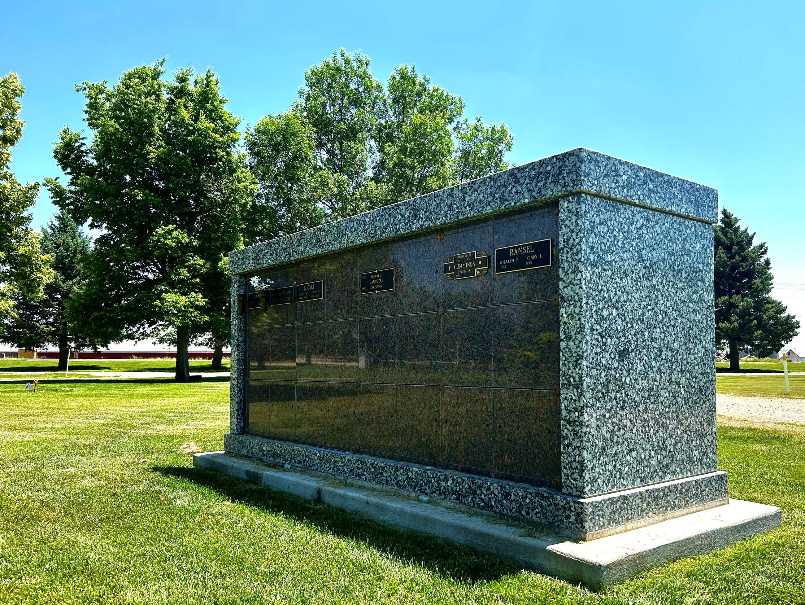 Granite columbarium on green lawn with trees in background. 
